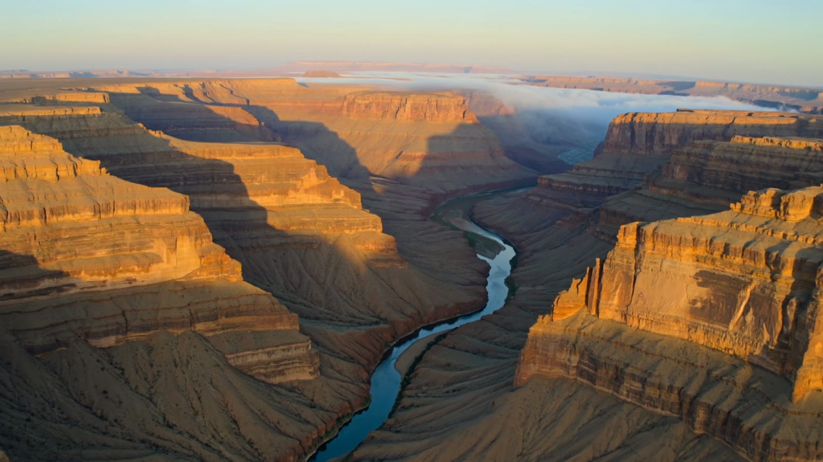 A sweeping aerial view over a dramatic canyon at golden hour with a winding river below, a still from an AI-generated drone clip.