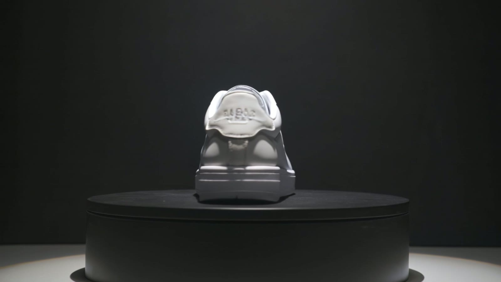 A modern white sneaker rotating on a pedestal in a dark studio with a dramatic spotlight and glossy reflections, a still from an AI-generated sneaker clip.