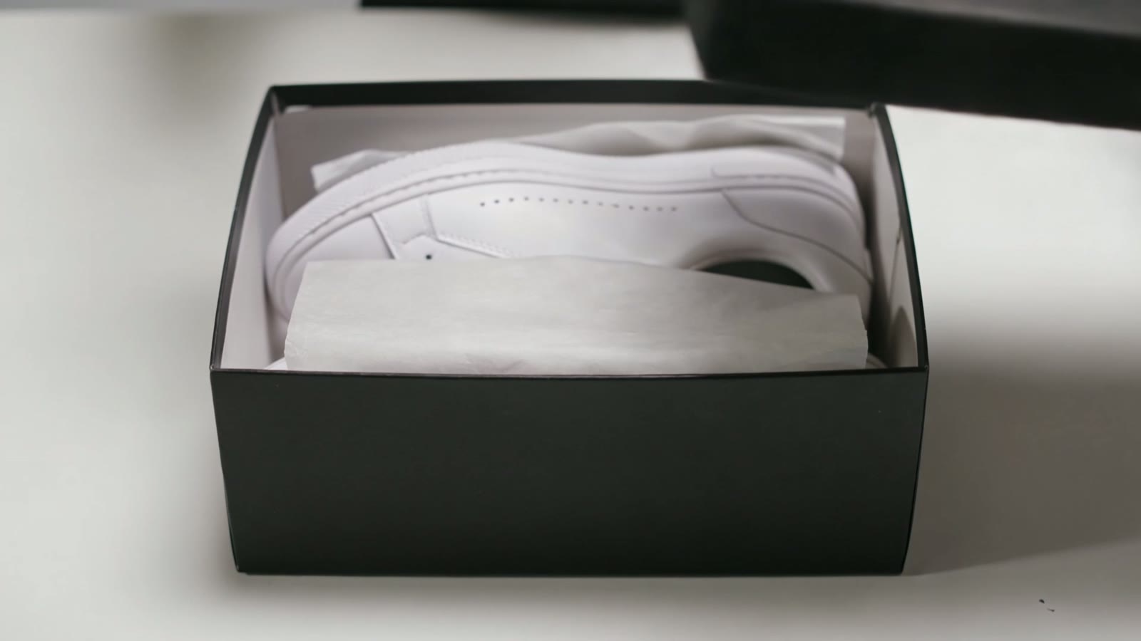 Hands lifting the lid of a premium box to reveal white sneakers in tissue paper, a still from an AI-generated unboxing clip.